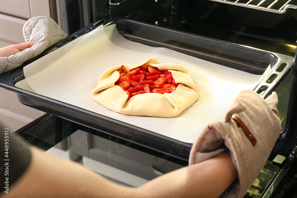 Woman putting baking tray with uncooked strawberry galette in oven