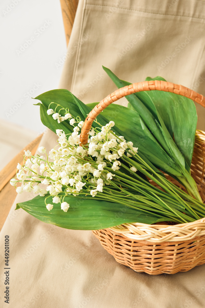 Basket with lily-of-the-valley flowers on chair, closeup