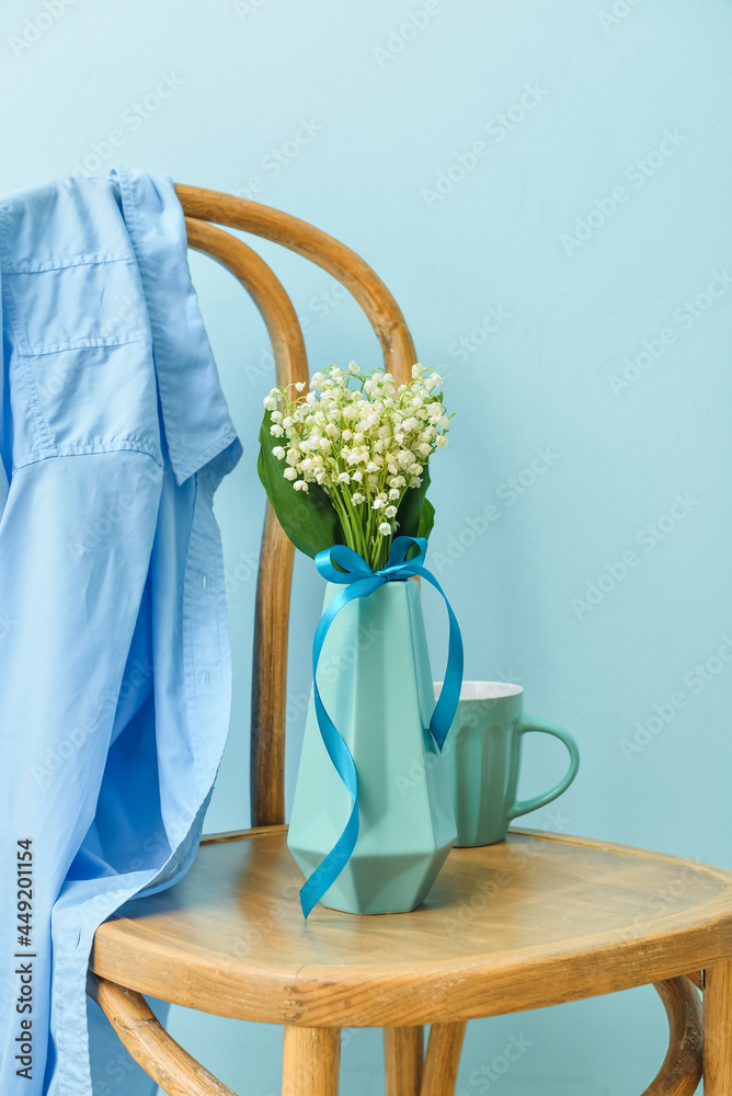 Vase with lily-of-the-valley flowers and cup of coffee on chair