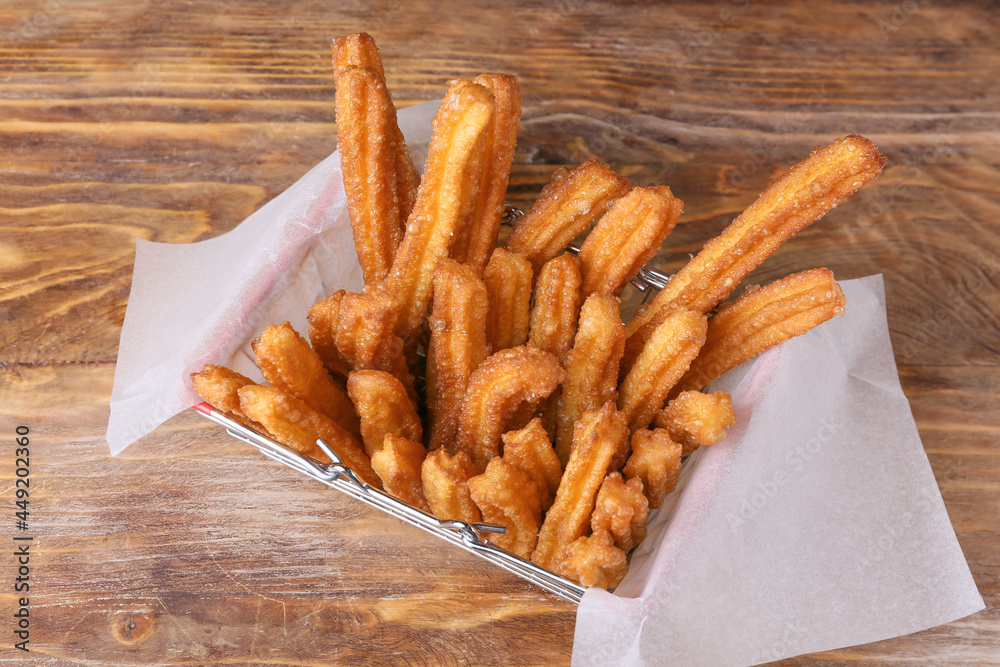 Basket with tasty churros in parchment on wooden background