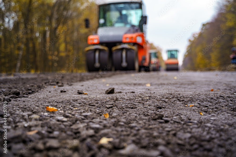 工人在道路施工期间操作沥青摊铺机。压路机工作近景