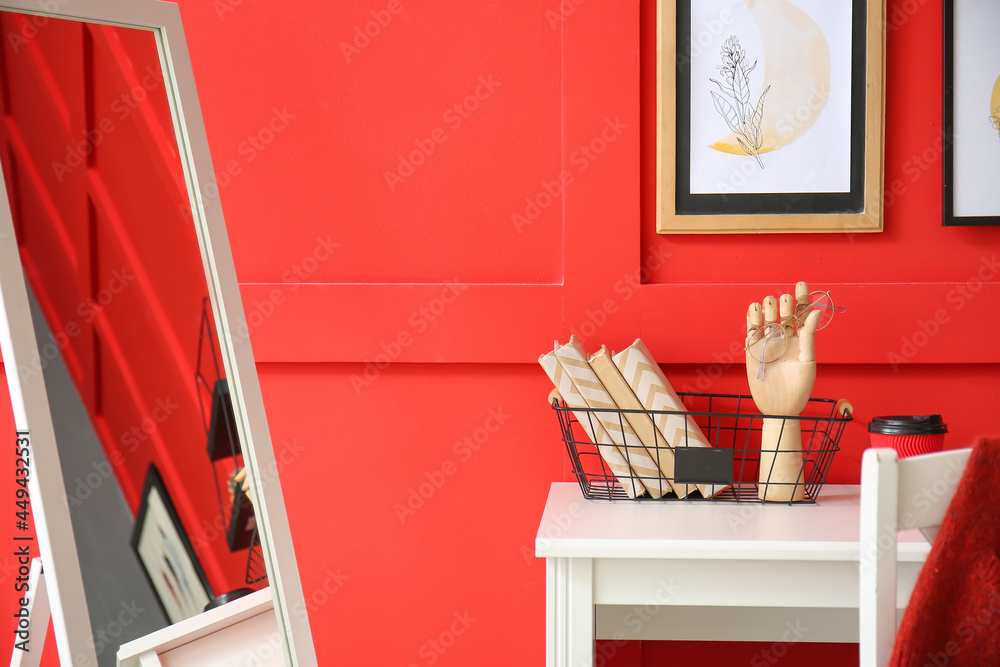 Wooden hand with eyeglasses and books on table near color wall