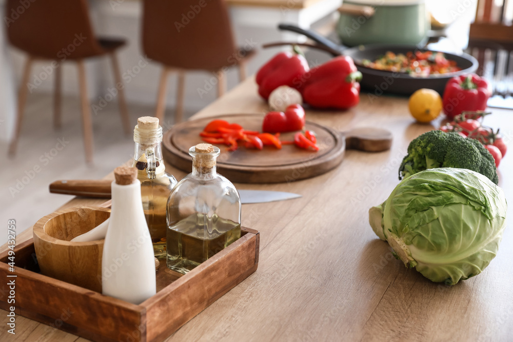 Bottles with oil and fresh vegetables on table in kitchen