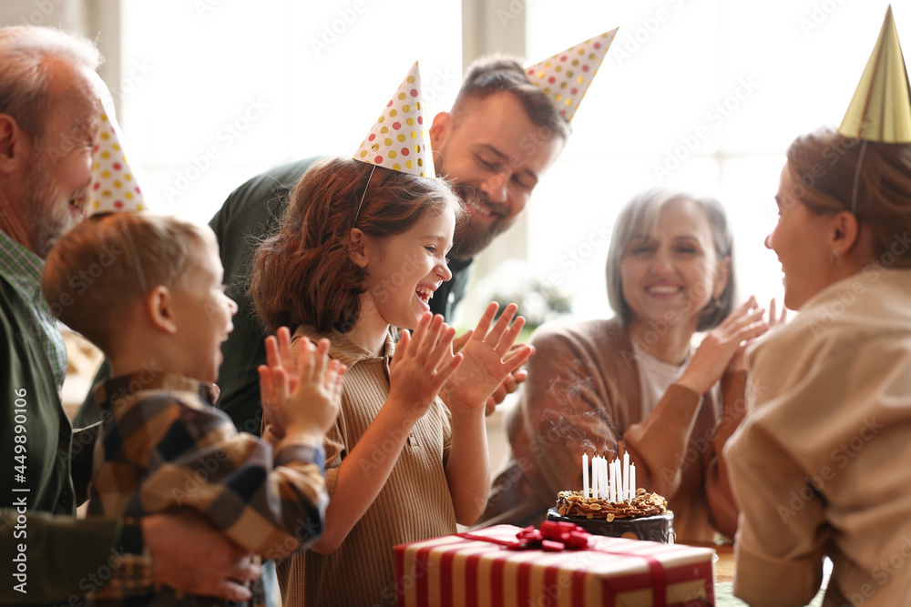 戴着派对帽的快乐大家庭在家庆祝小女孩生日时拍手