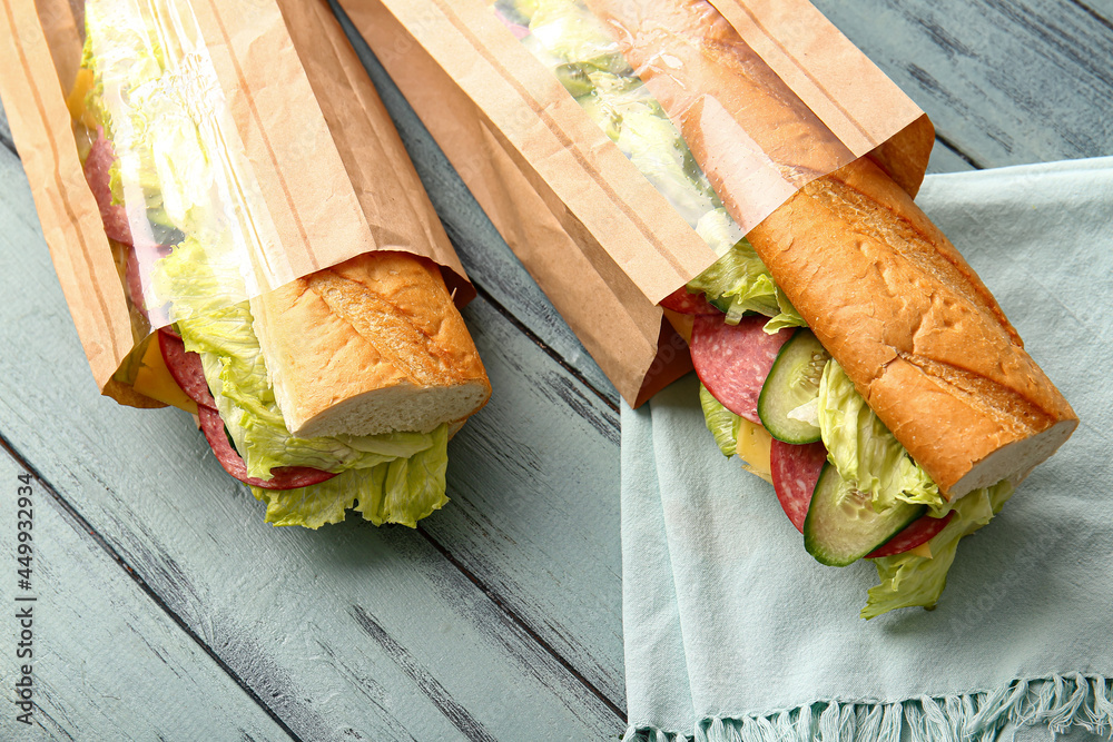 Bags with tasty sandwiches on color wooden background