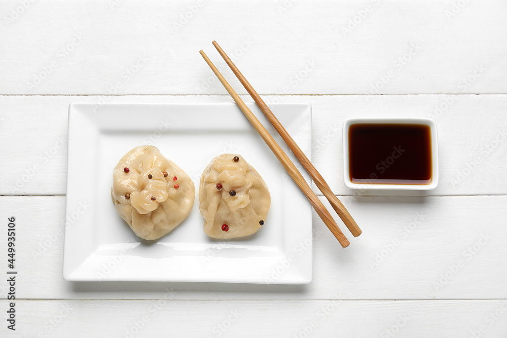 Plate with tasty dumplings, chopsticks and bowl of sauce on light wooden background