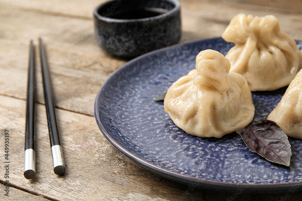 木制背景上的盘子里有美味的饺子、筷子和一碗酱汁，特写