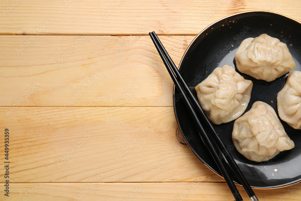 Plate with tasty dumplings and chopsticks on wooden background