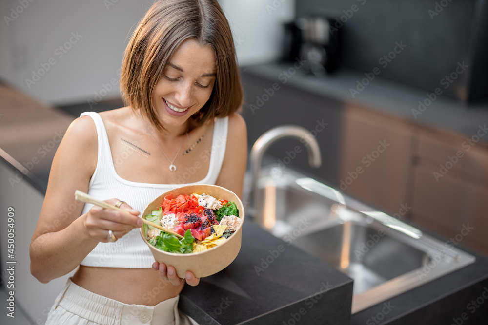 Young woman eating healthy asian bowl with tuna and salad on the modern kitchen at home. Healthy tak