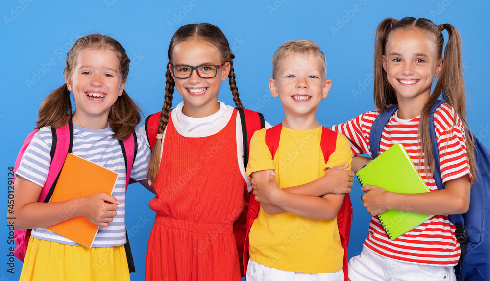 Happy children, girls and boys, standing with backpacks behind and exercise books, smiling at camera