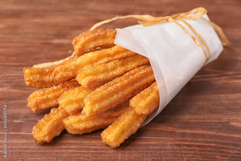 Tasty churros in parchment on wooden background, closeup