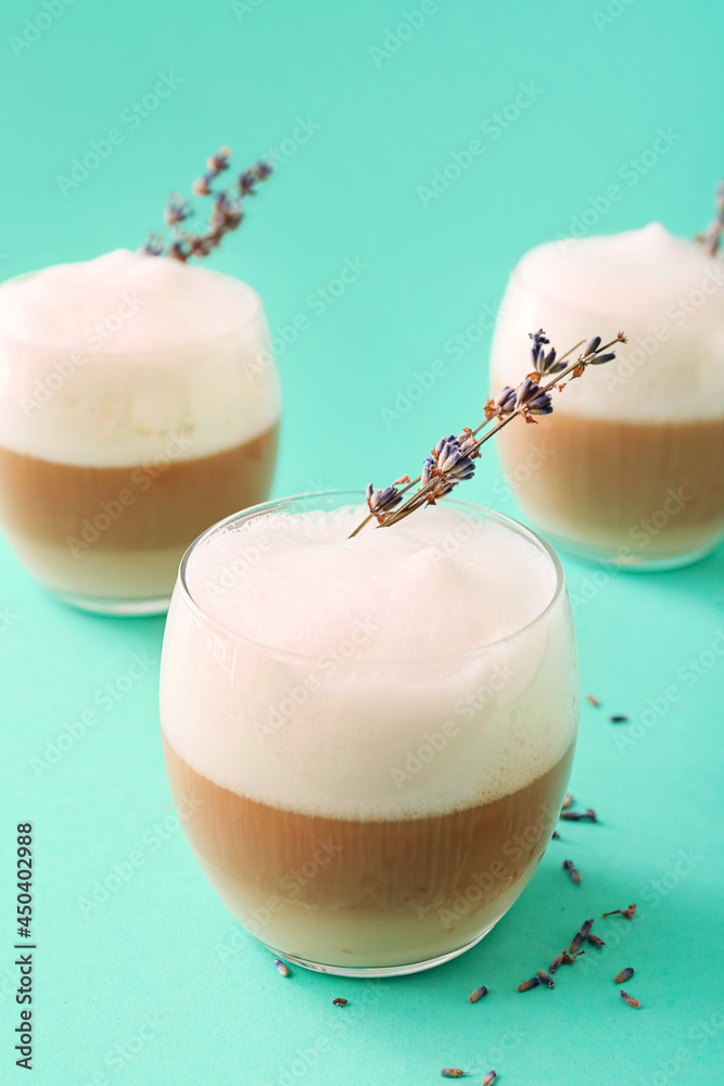 Glasses of tasty lavender latte and flowers on color background