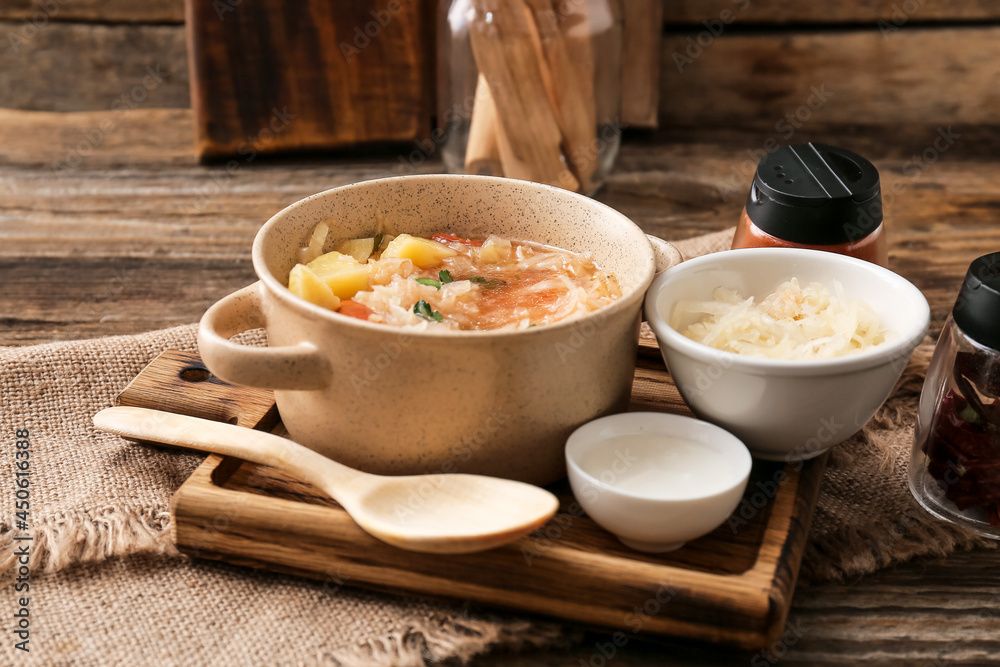 Pot with tasty sauerkraut soup and sour cream on wooden background