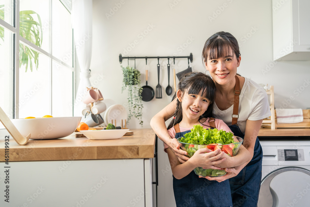 亚洲母亲与女儿站在一起，拿着蔬菜碗的肖像。