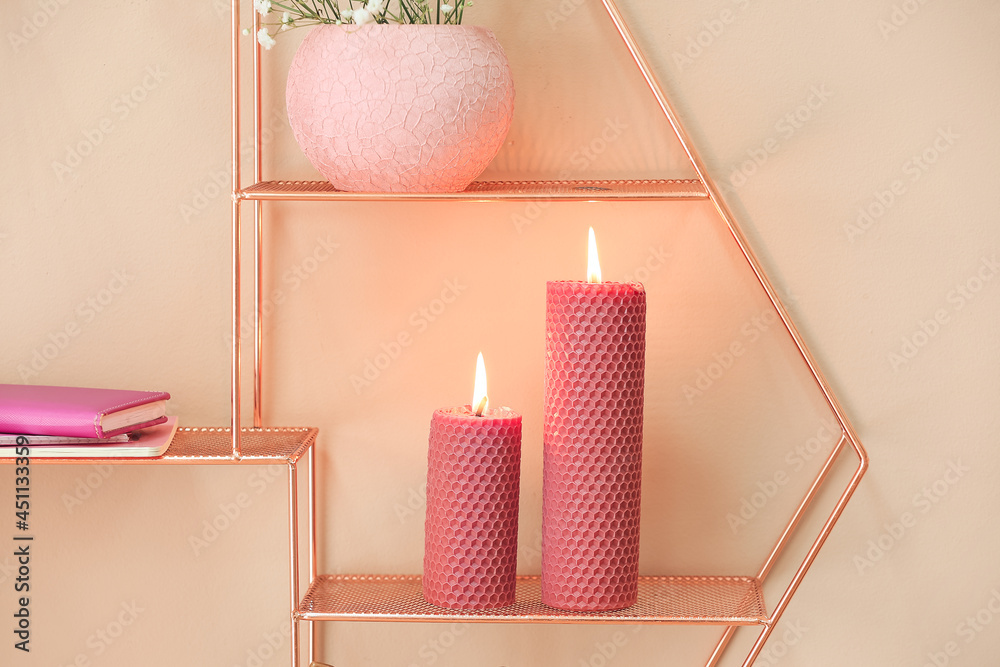 Shelves with burning candles on color wall