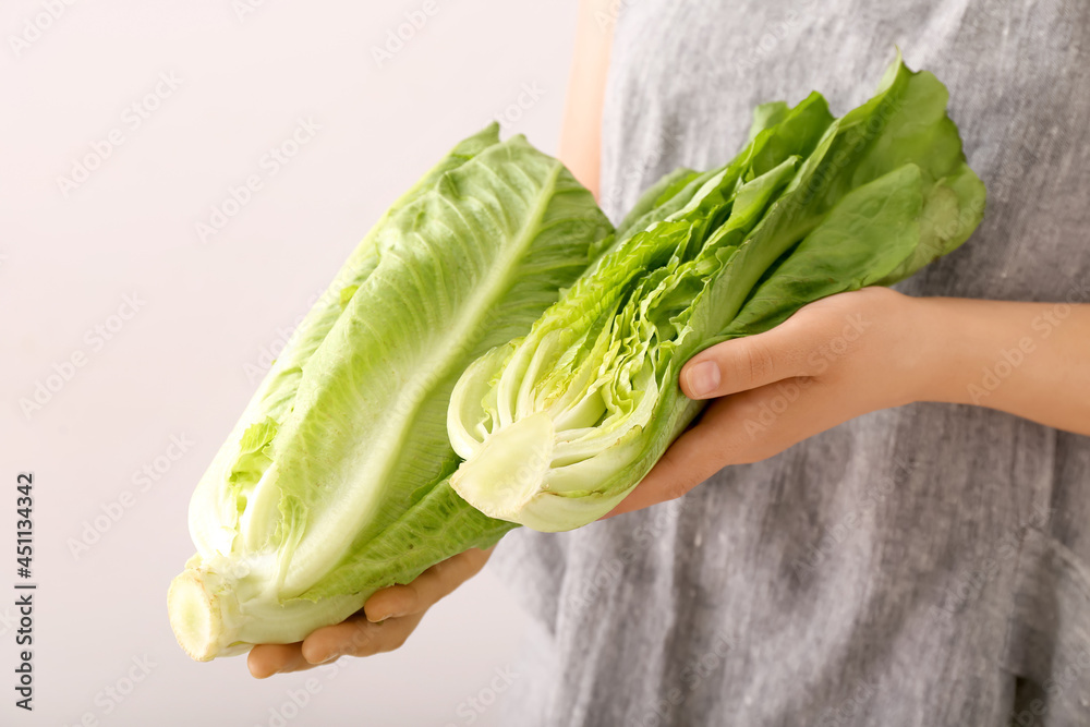 Woman with fresh romaine lettuce on light background, closeup