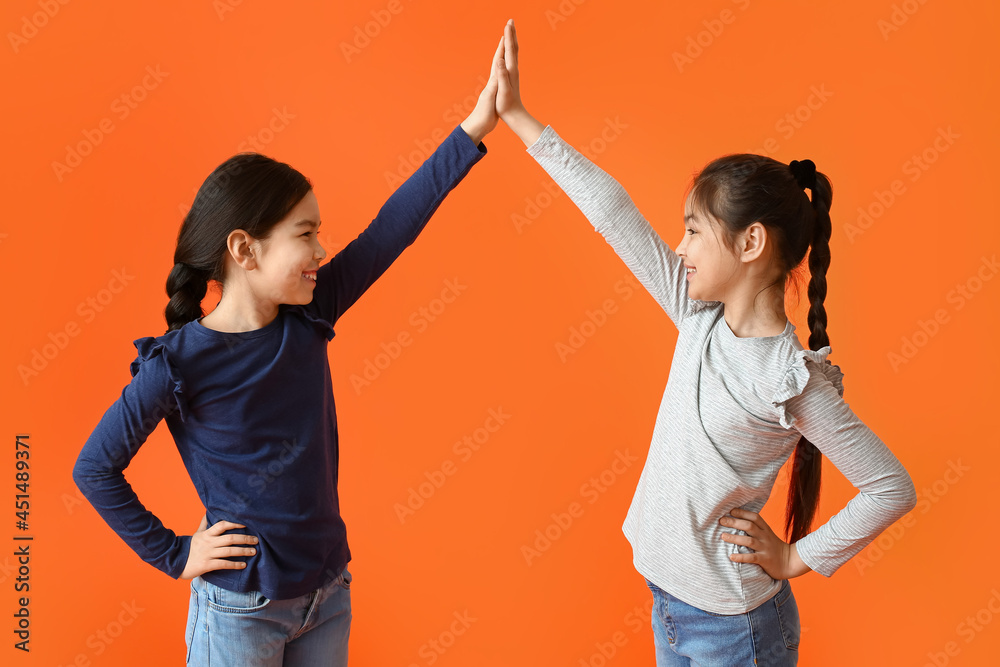 Cute little sisters giving each other high-five on color background