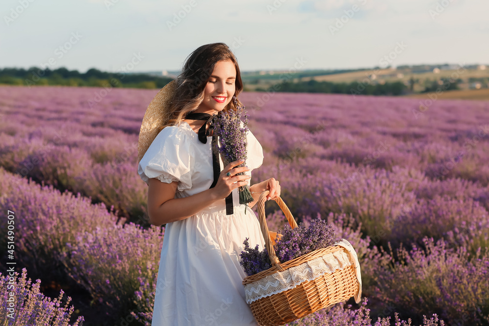 Beautiful young woman with basket for picnic in lavender field