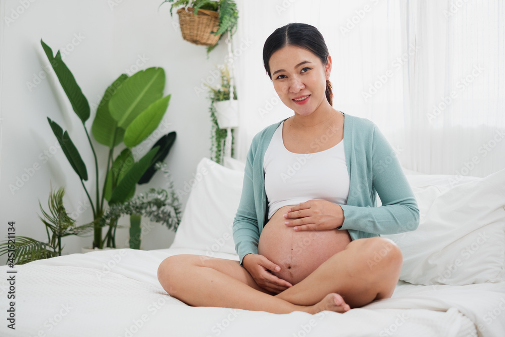 床上的亚洲年轻孕妇在卧室里大肚子微笑