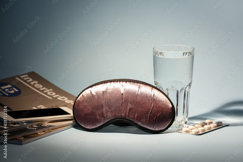 Sleeping mask with pills and glass of water on color background