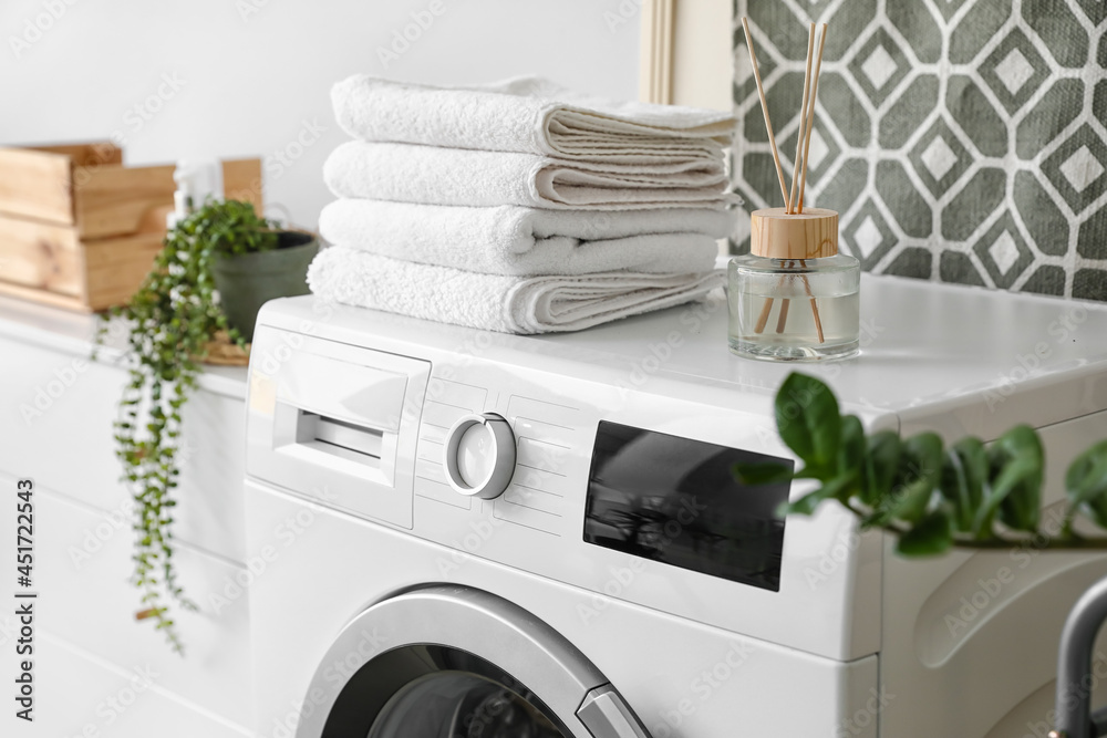 Modern washing machine with towels and reed diffuser in bathroom