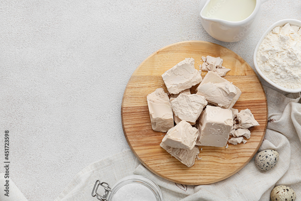 Wooden board with fresh yeast on light background