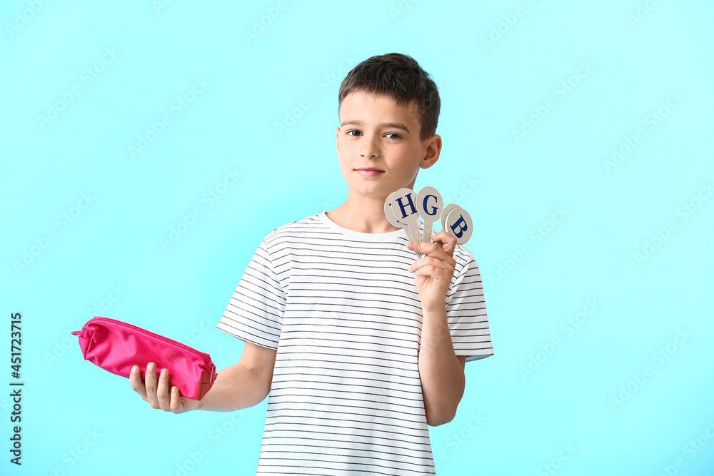 Little boy with pencil case and set of letters on color background