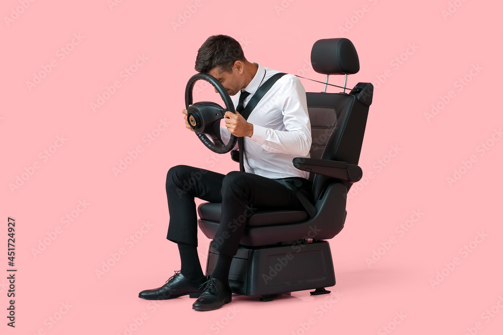 Stressed businessman in car seat and with steering wheel on color background