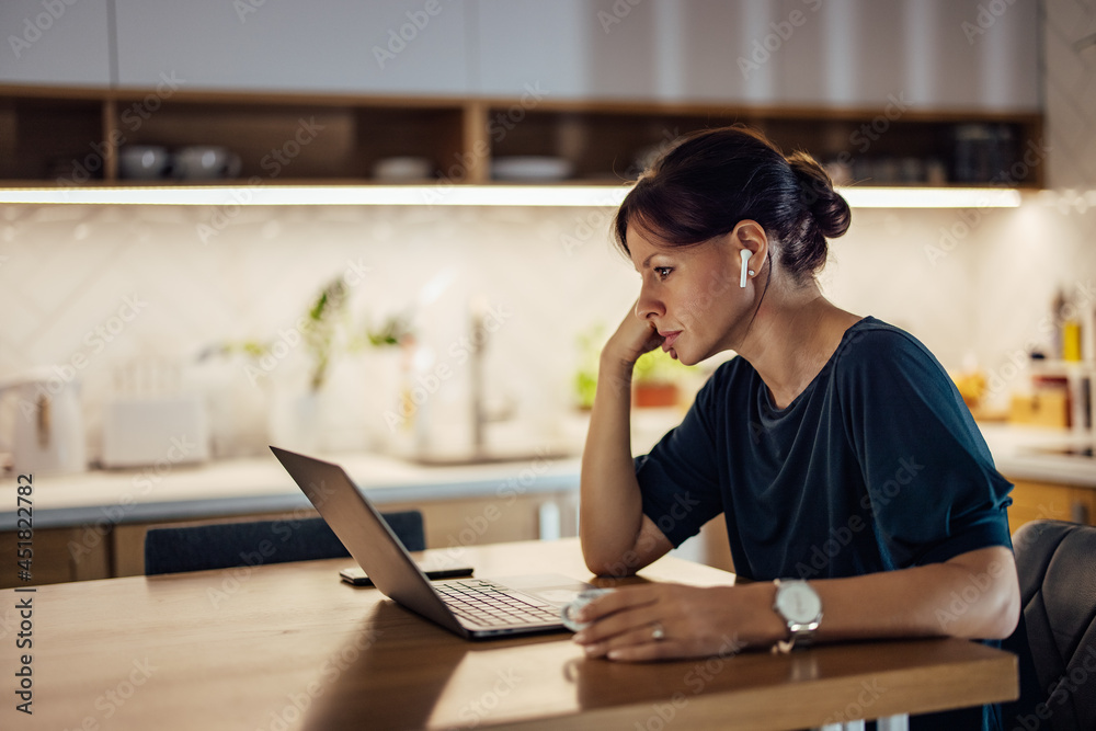 Tired businesswoman looking at laptop while working late, at home.