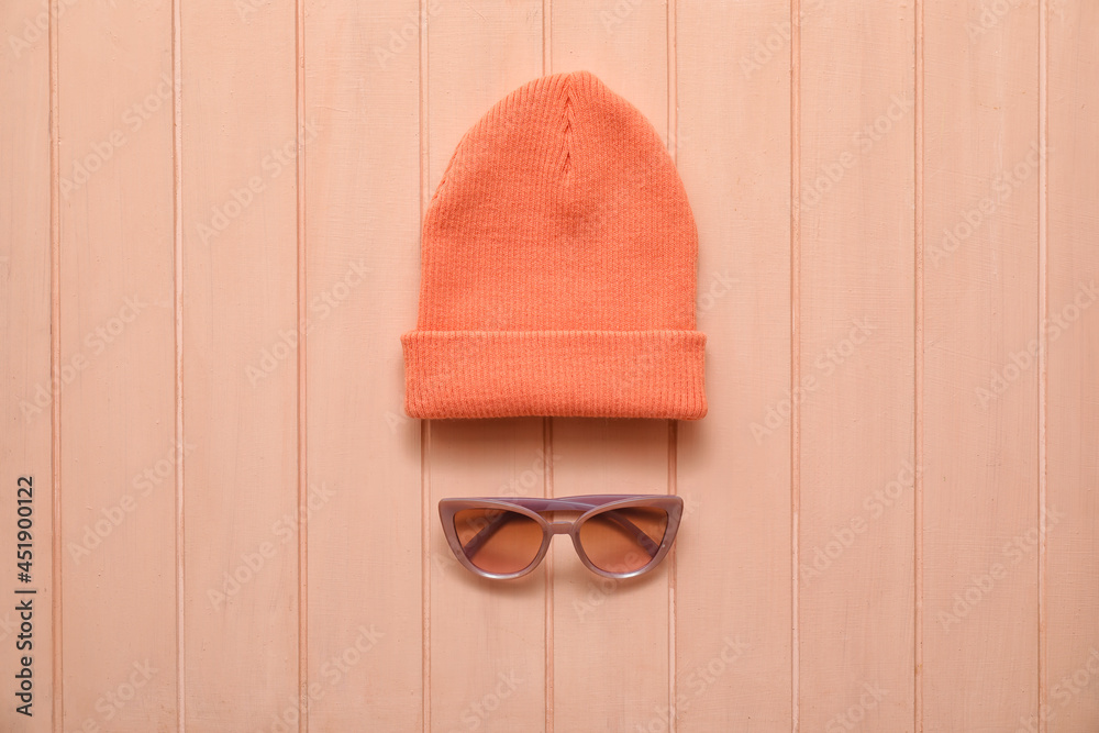 Stylish warm hat and sunglasses on color wooden background