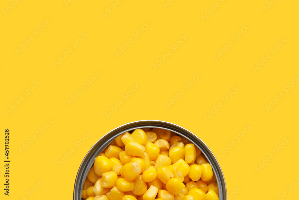 Opened tin can of corn kernels on color background