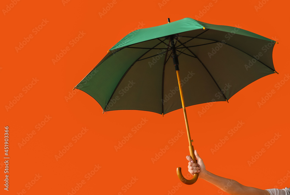 Female hand with open umbrella on color background