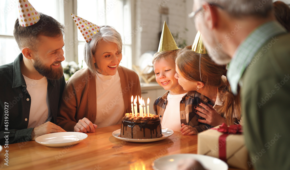 Happy little boy celebrating birthday with family at home, looking at cake with lit candles