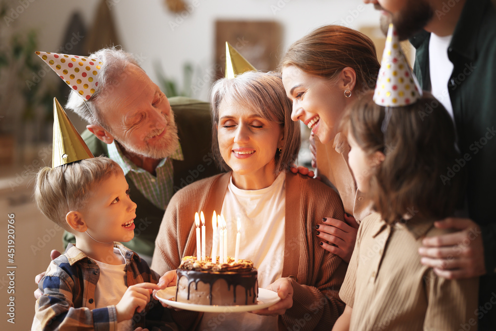 Happy senior woman holding cake with burning candles while celebrating birthday with big lovely fami