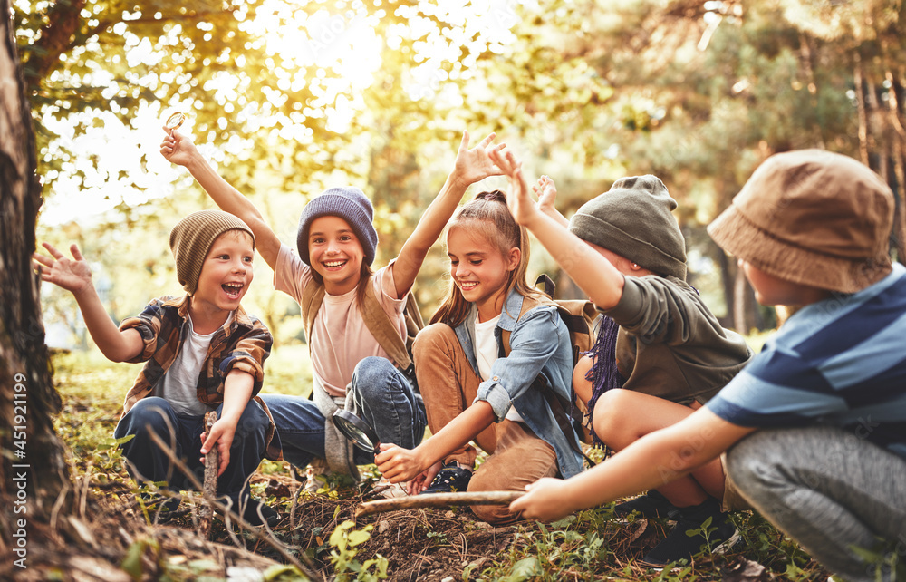 Happy school kids scouts learning how to create fire with magnifying glass and sun in forest