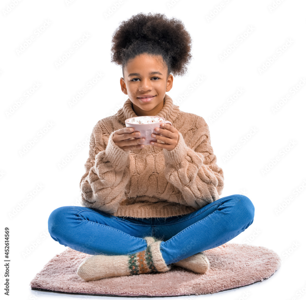 African-American teenage girl with cup of hot cacao sitting on carpet against white background