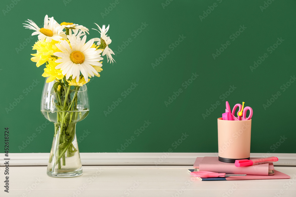 Vase with flowers and stationery on table in classroom. Teachers Day celebration