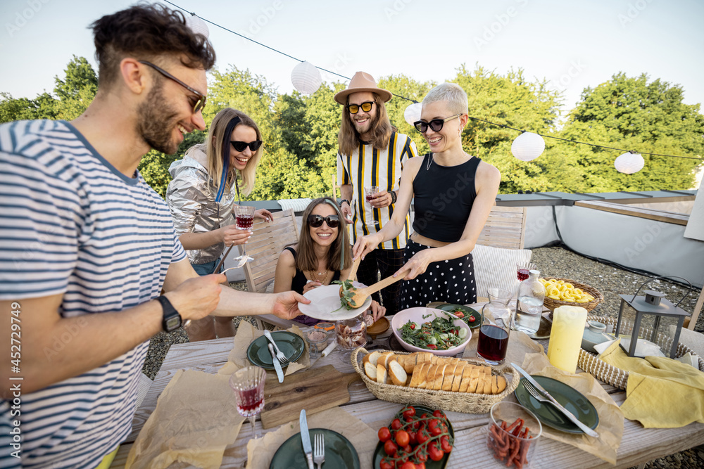 Young stylish friends have a festive dinner outdoors, share healthy food, have great summer time tog