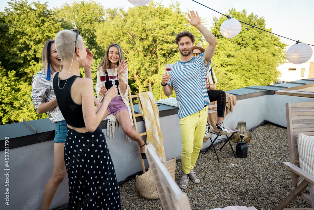 Young stylish friends having fun, hanging out and drinking wine at party on the rooftop terrace