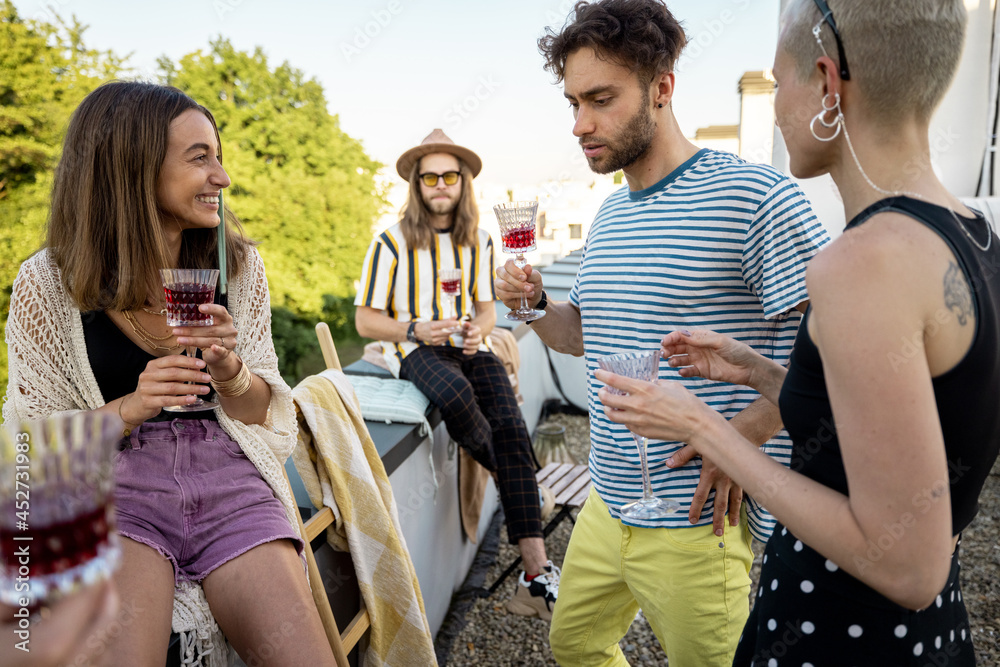 Young stylish friends having fun, hanging out and drinking wine at party on the rooftop terrace