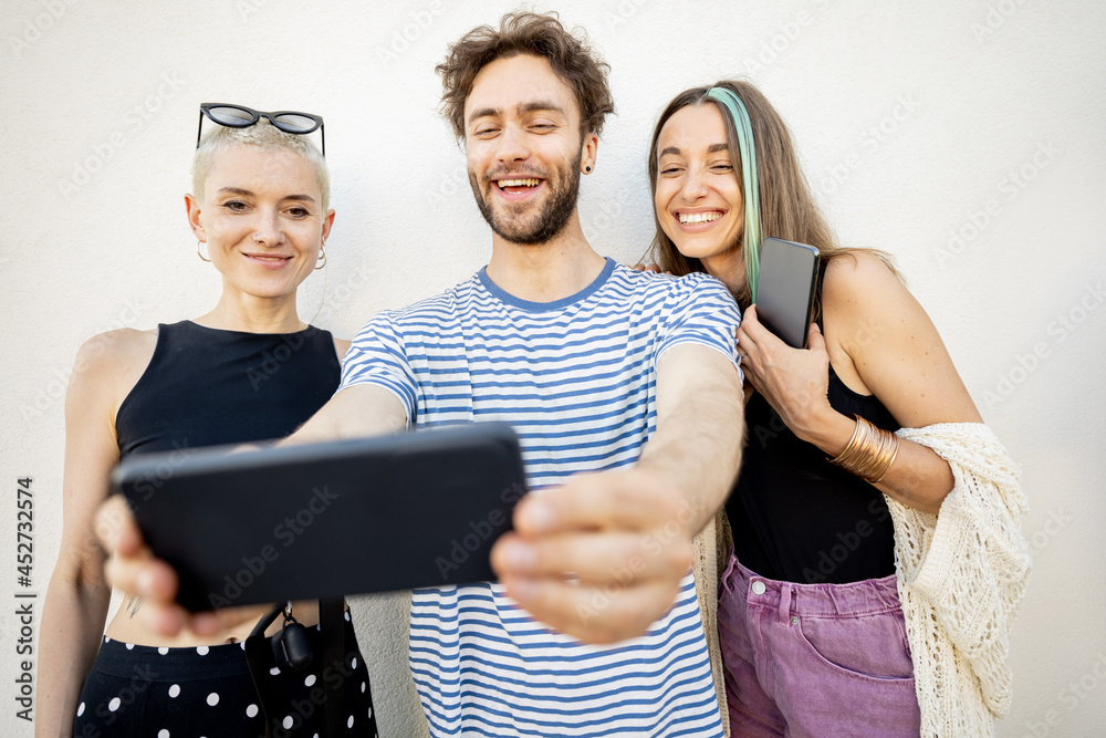 Young stylish friends have fun, taking selfie photo on phone on a white background. Millennials or g