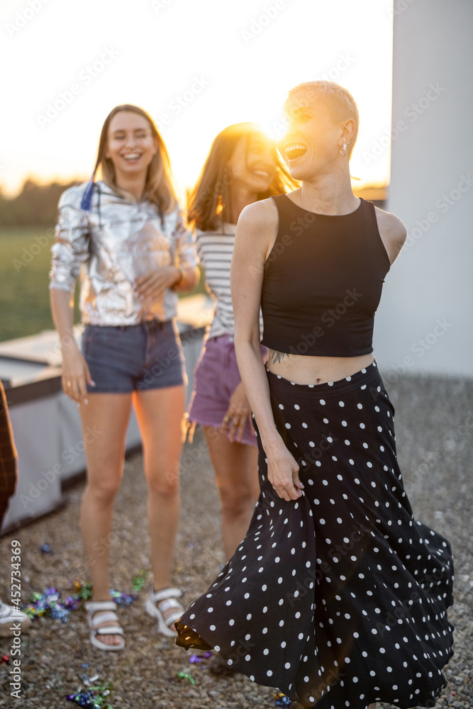 Young stylish friends dancing outdoors, having party at rooftop terrace on sunset