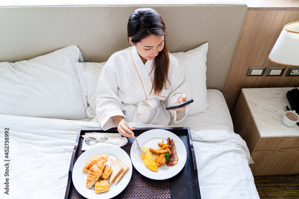 Portrait beautiful young Asian woman wearing bathrobe using smartphone while eating breakfast on a b