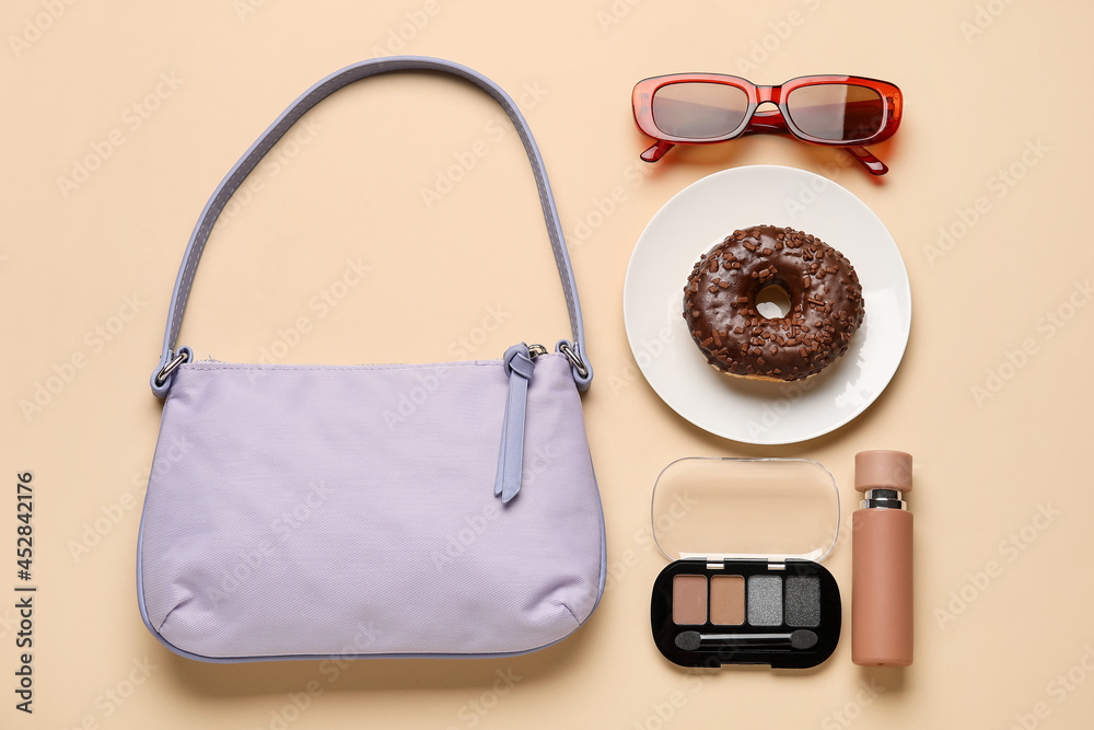 Composition with trendy handbag, plate with doughnut and accessories on color background