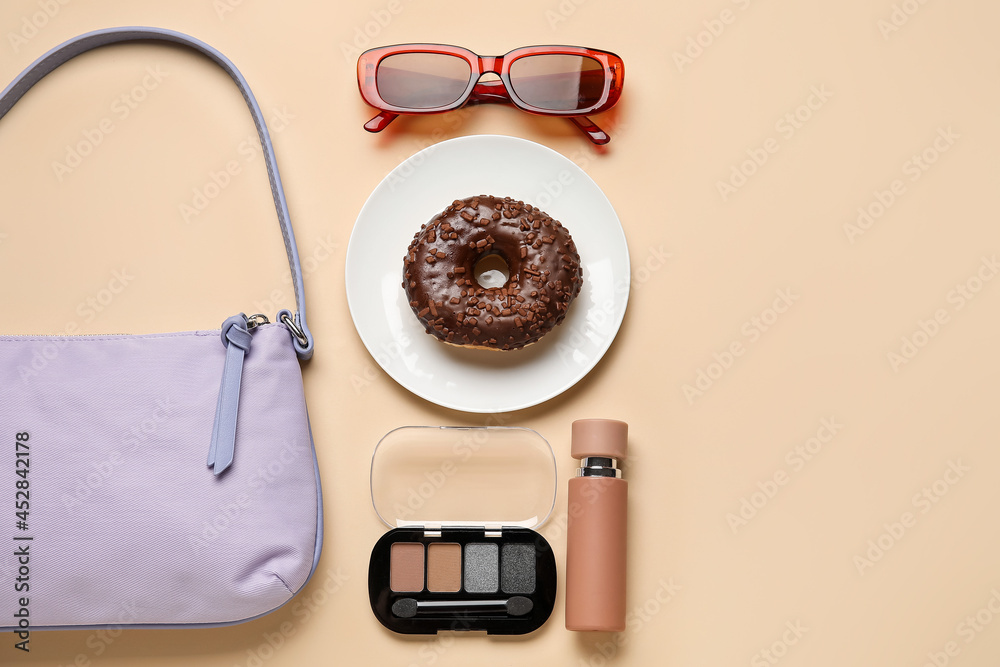 Composition with trendy handbag, plate with doughnut and accessories on color background