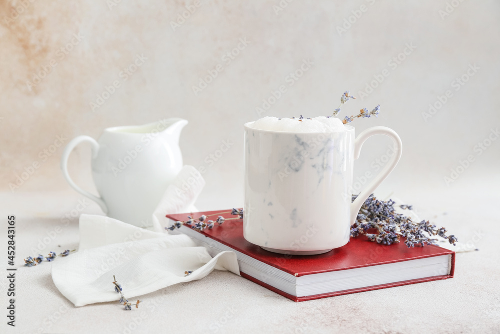 Cup of tasty lavender latte, book and flowers on light background