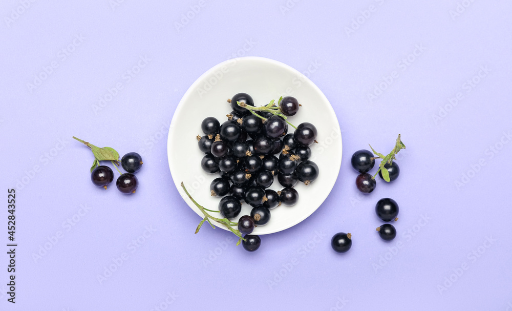 Plate with ripe black currant on color background