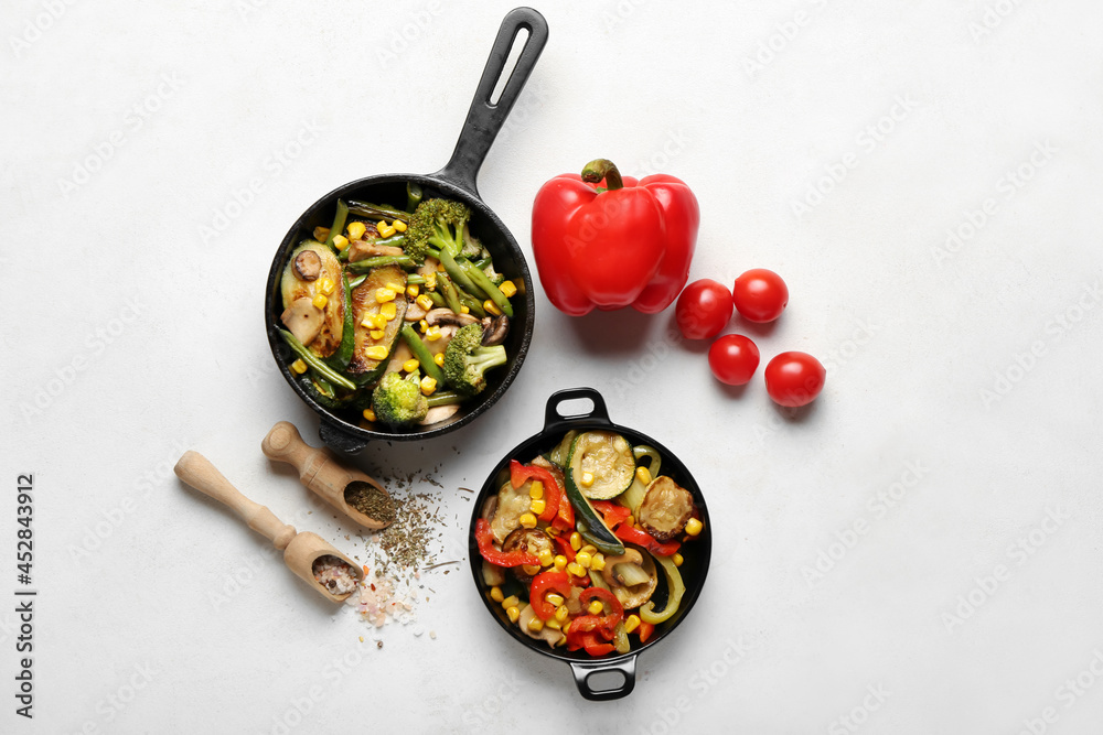 Frying pans with different vegetables and spices on light background