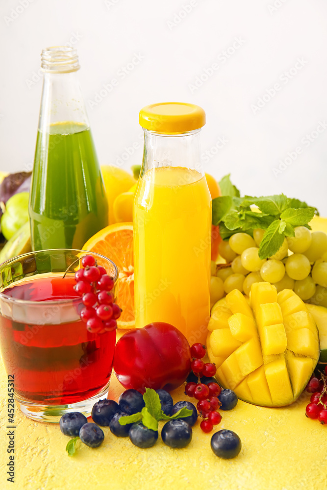 Bottles with healthy juice, fruits and vegetables on light background