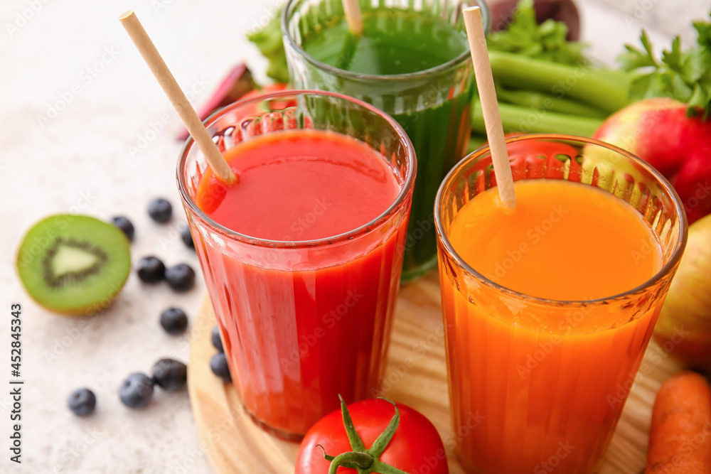 Glasses with healthy juice, fruits and vegetables on light background